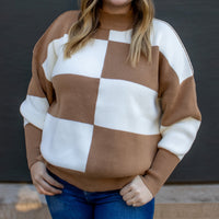 Woman wearing a checkered sweater with brown and white colors against a dark background