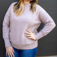 Woman wearing a light pink sweater and blue jeans against a dark background