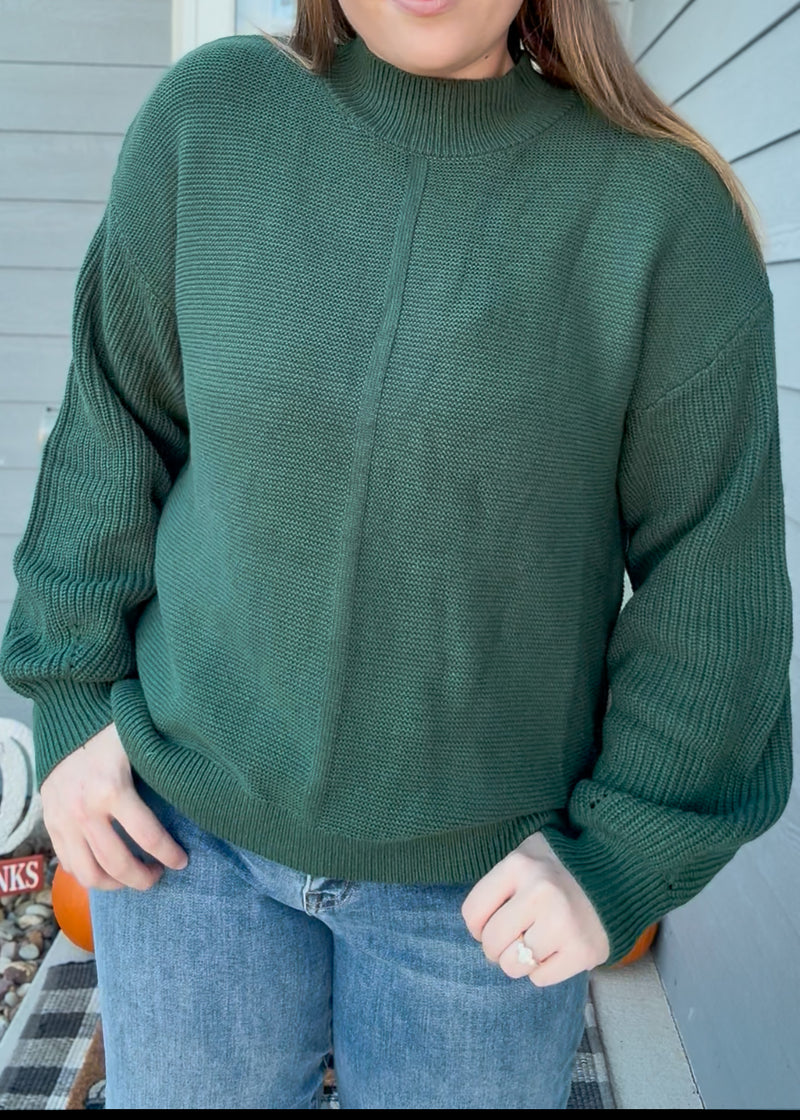 Person wearing a green sweater and blue jeans with a neutral background
