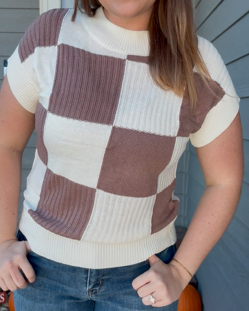 Person wearing a checkered sweater with brown and white squares.